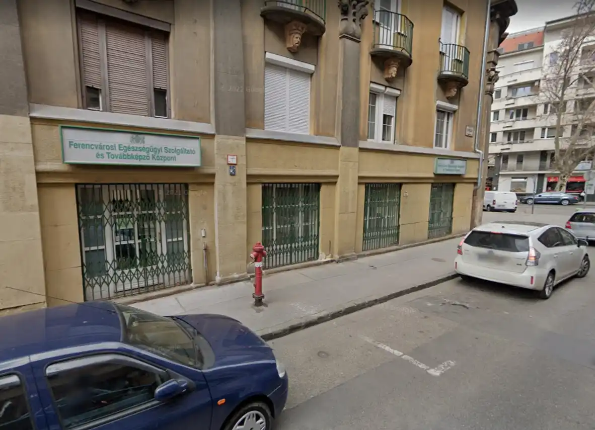 Többemeletes lakóépület földszinti üzlethelyiséggel és parkoló autókkal.